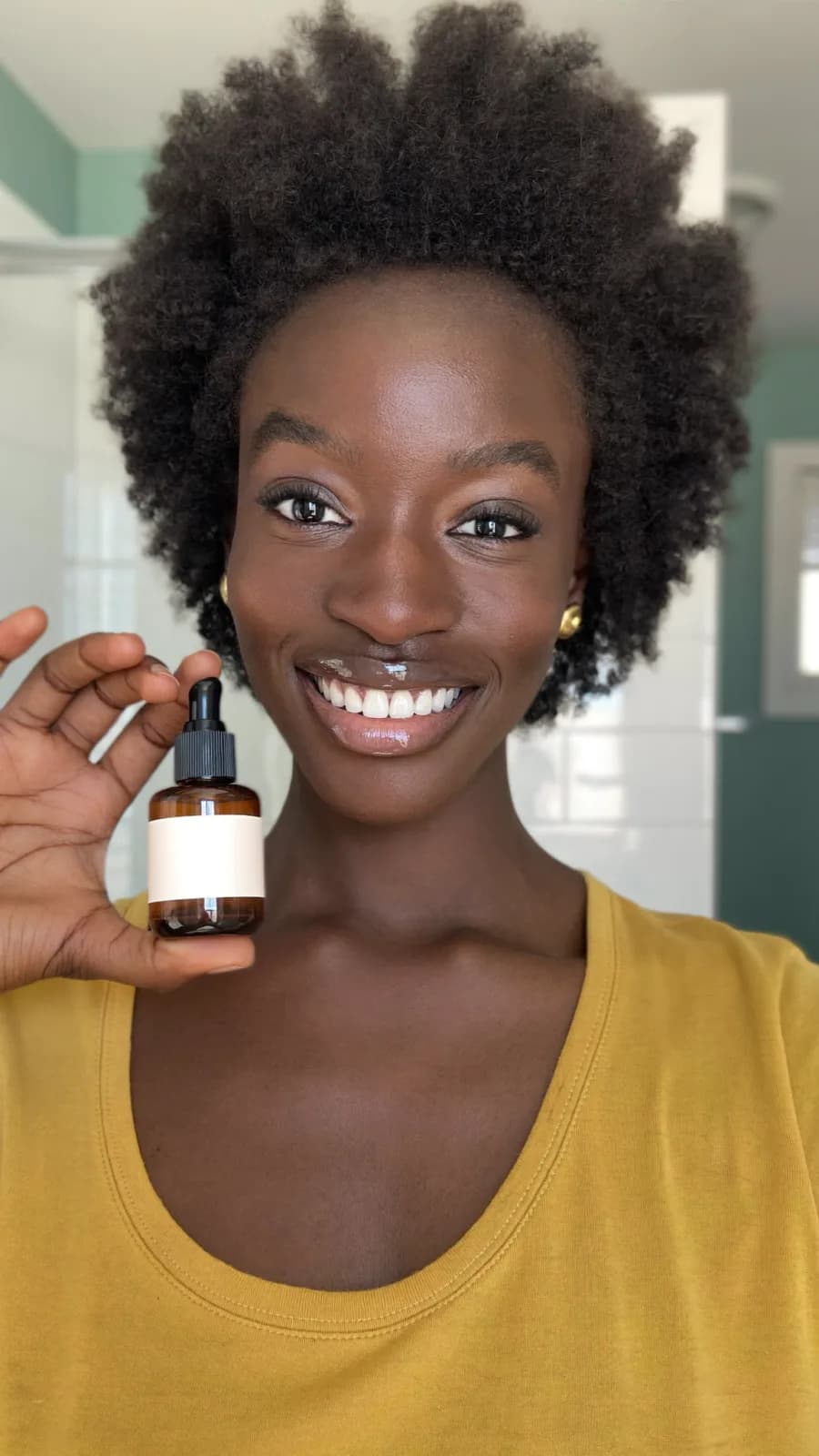 Smiling creator in a yellow top holding a small amber dropper bottle in her living room