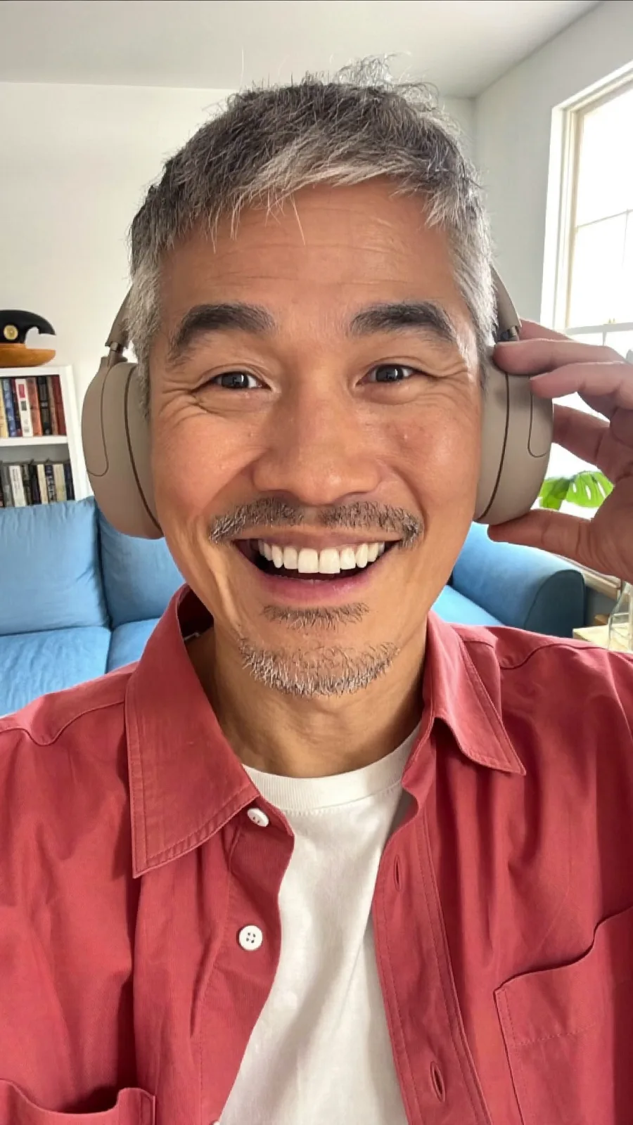 Grey-haired creator in a red shirt smiling with headphones on in his living room