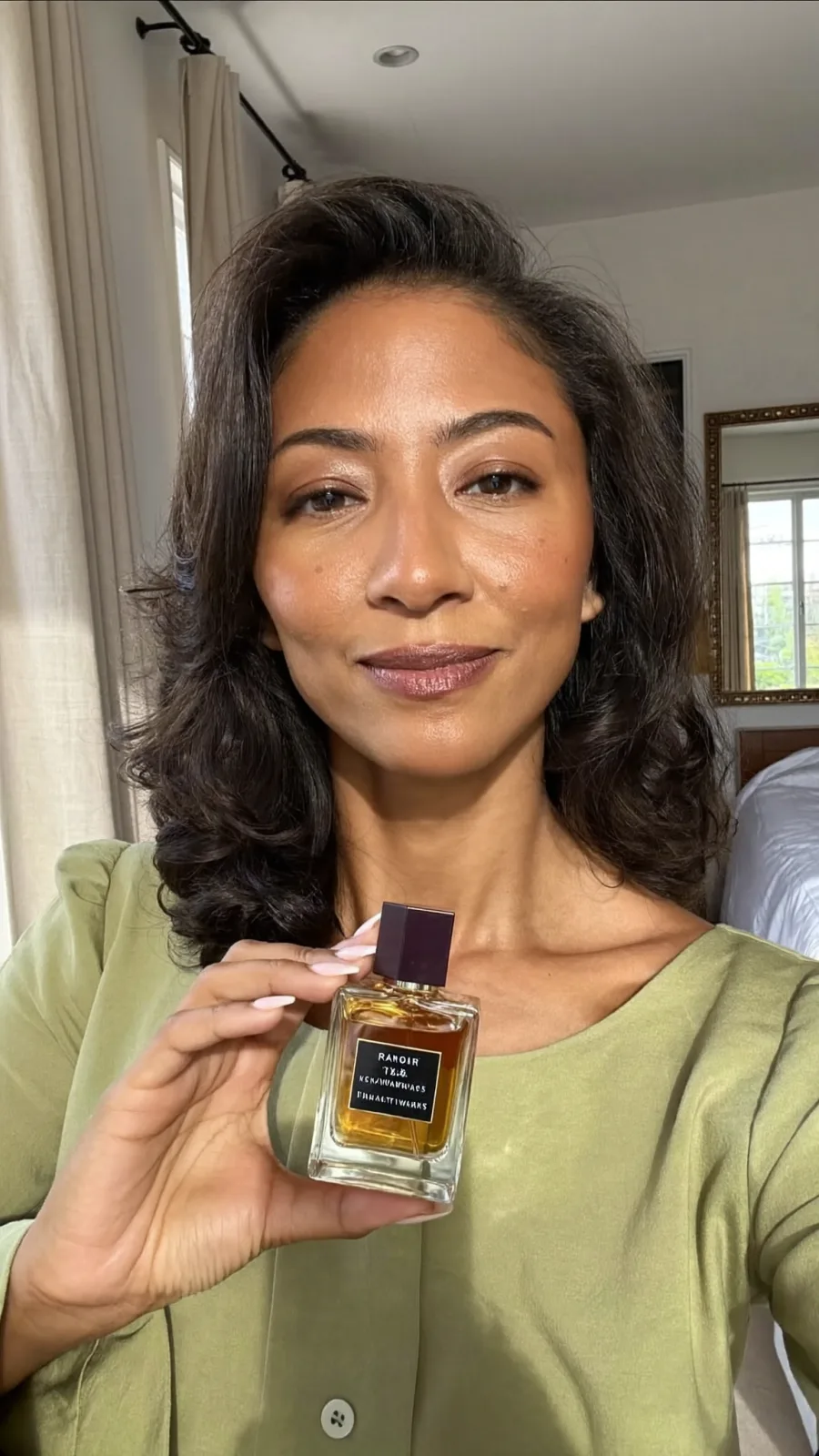 Creator in a sage blouse holding a square perfume bottle up to the camera
