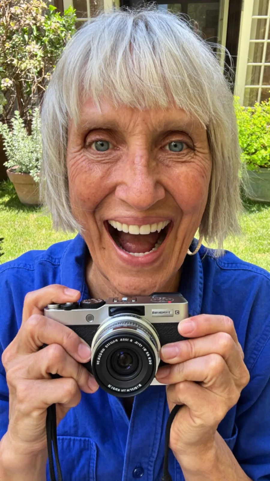 Grey-haired woman in a blue shirt holding a compact camera up to her eye line