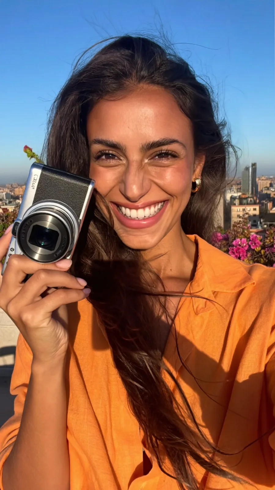 Creator in an orange shirt holding a compact camera on a sunny rooftop