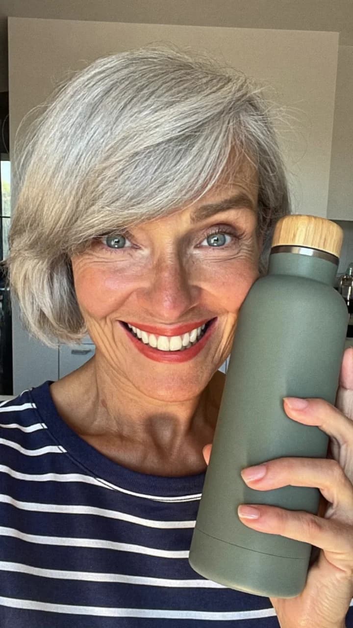 Grey-haired woman in a striped top smiling with a sage bottle at home
