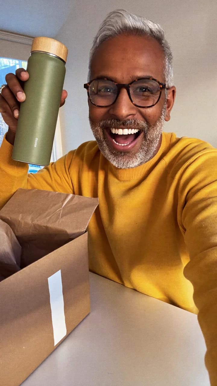 Smiling man in a yellow sweater with a sage bottle and an open delivery box