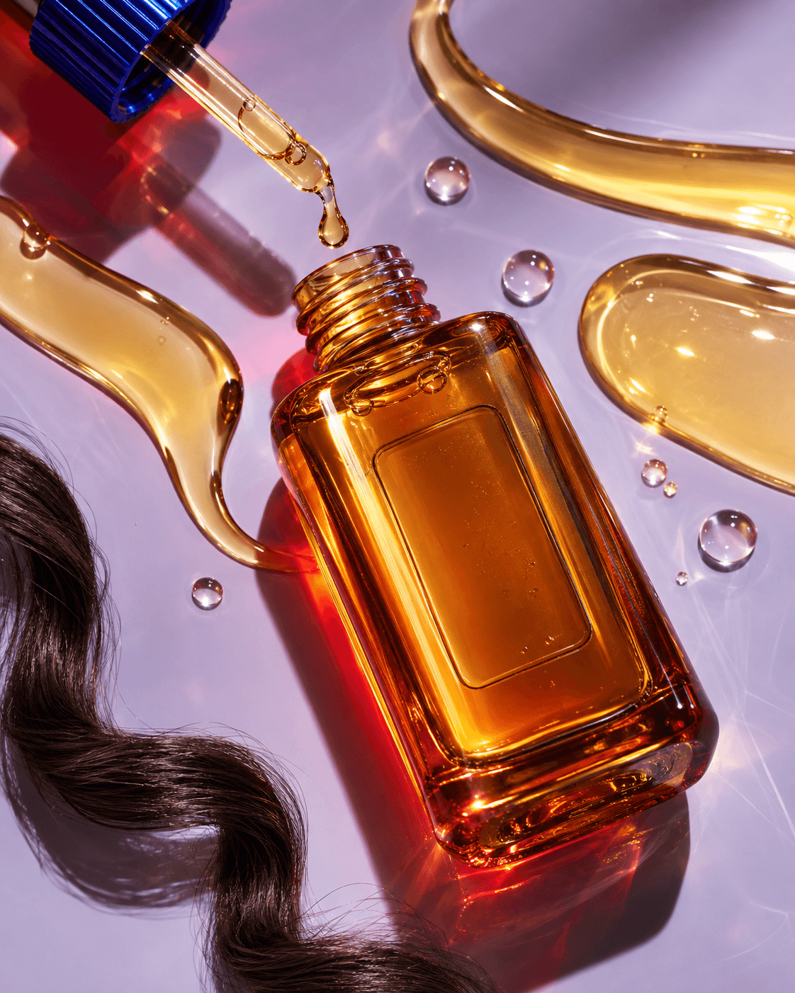 Amber hair oil bottle and dropper spilling golden serum beside a dark curl