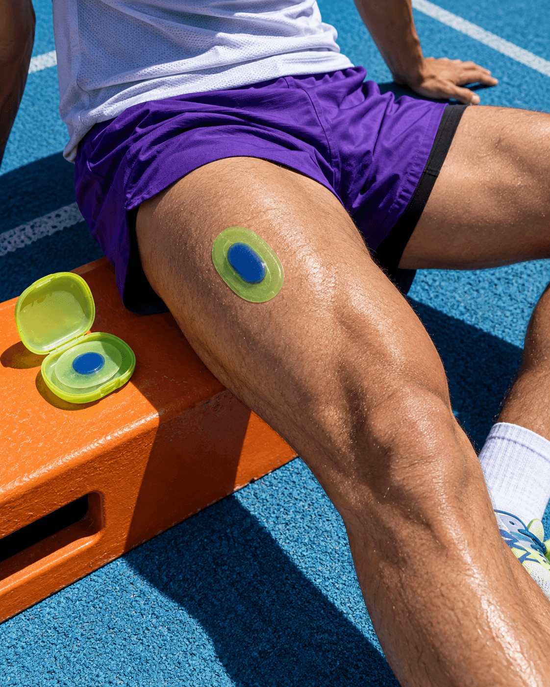 Green and blue recovery gel patch applied to a runner's thigh, open case beside it