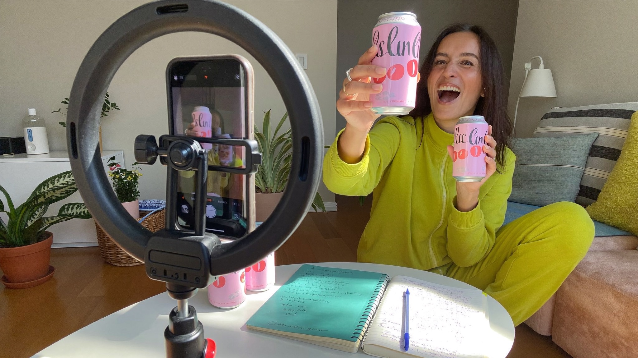 An expressive creator presenting pink drink cans to a phone camera.