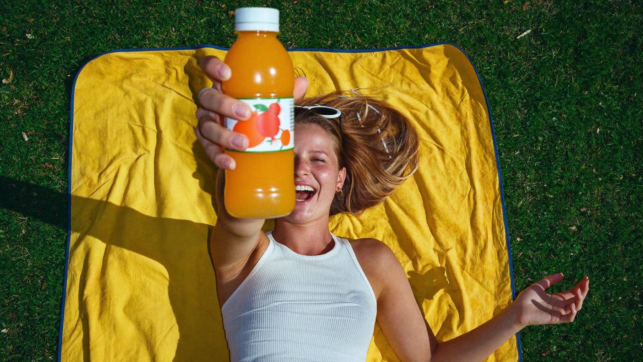 An overhead view of a creator holding juice on a yellow picnic blanket.