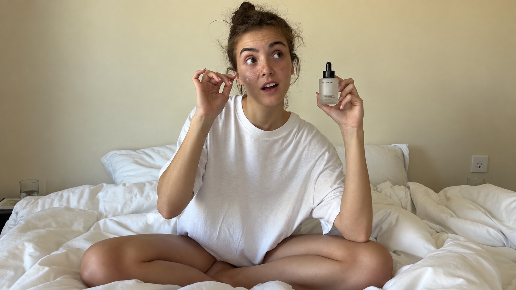 A creator presenting a skincare serum while sitting on her bed.